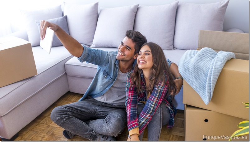 Cheerful and happy young couple making a selfie in new home with moving cardboard box during move into new apartment